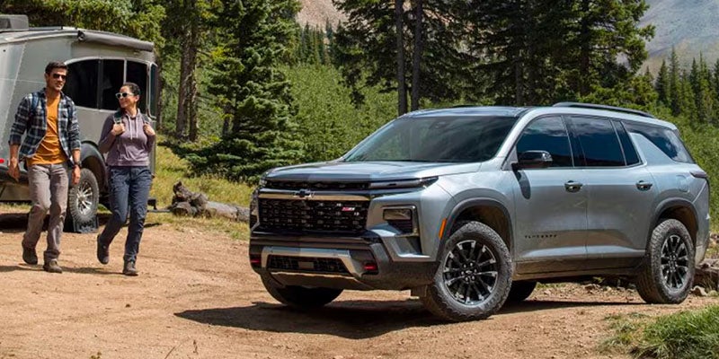 Chevrolet Traverse Parked In Woods With Camping Trailer in Background