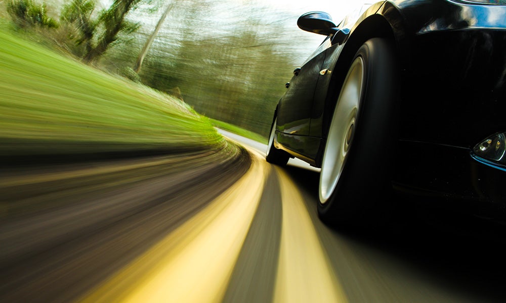 Closeup photo of car wheels on a road surrounded by greenery